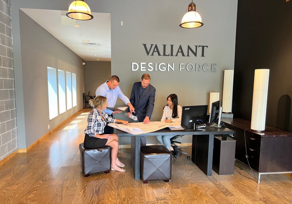 Two men and two women are sitting around a desk looking at blueprints