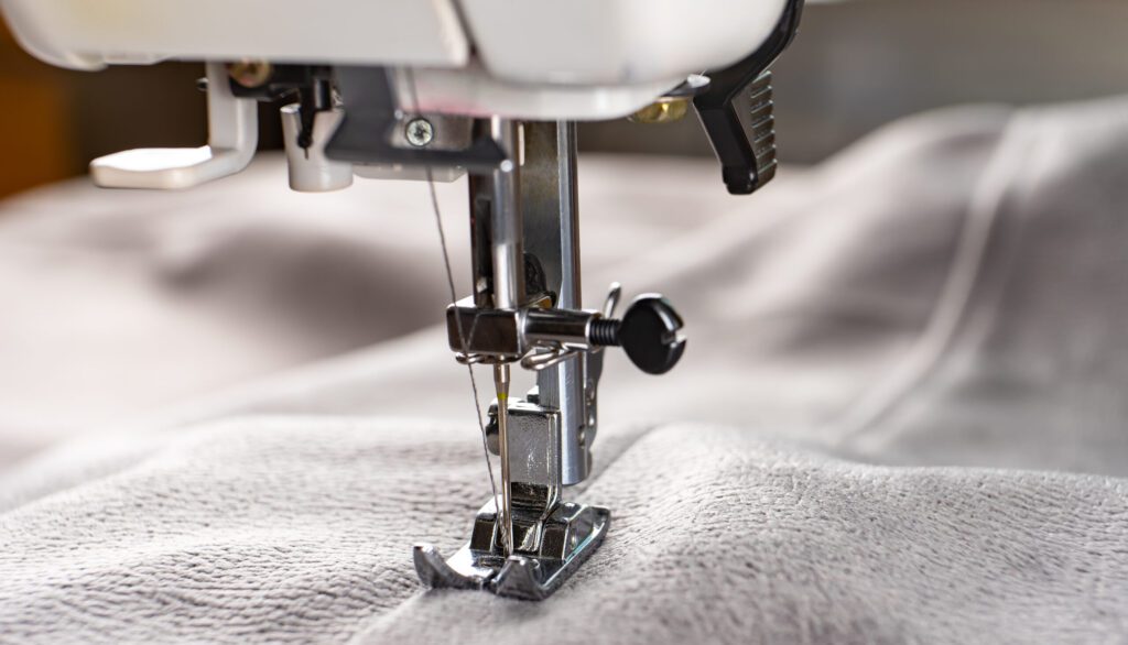 Modern sewing machine and gray fabric. Sewing process, handmade, hobby, DIY, business, repair Close up image of grey fabric on a modern sewing machine